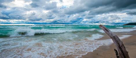 A beach with waves, a driftwood log, and a cloudy sky.