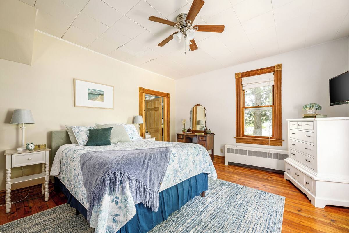 A bedroom with a bed, a nightstand, a dresser, a mirror, a ceiling fan, and a window.