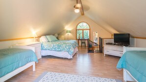 A spacious attic bedroom with a high ceiling, a large bed, a desk, and a TV. - The Cottonwood Inn B&B (Empire)