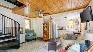 A cozy living room with a staircase, a sofa, a wooden bookshelf, and a kitchen area in the background. - The Cottonwood Inn B&B (Empire)
