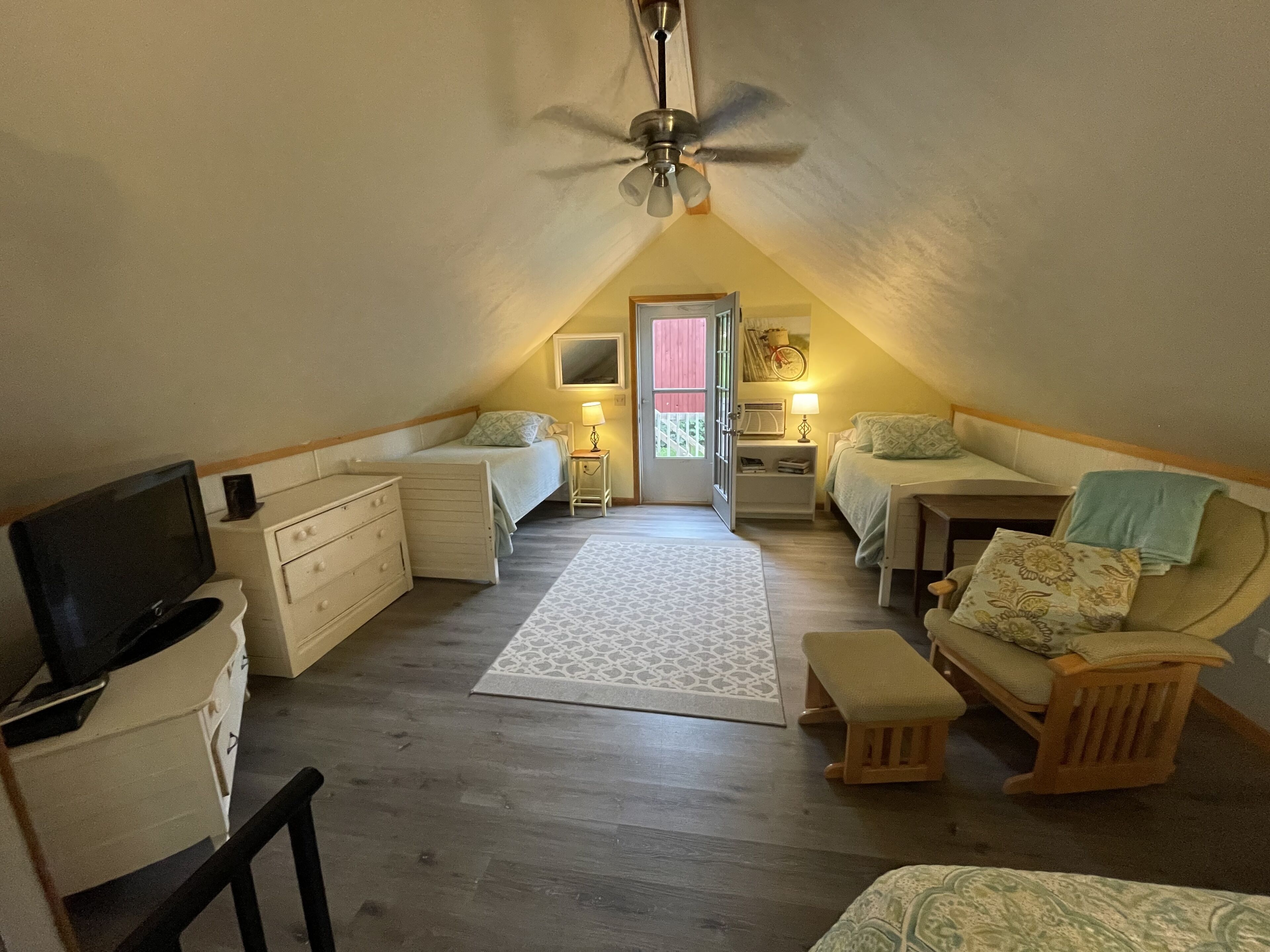 A cozy attic bedroom with a ceiling fan, two beds, a TV, and a small desk.