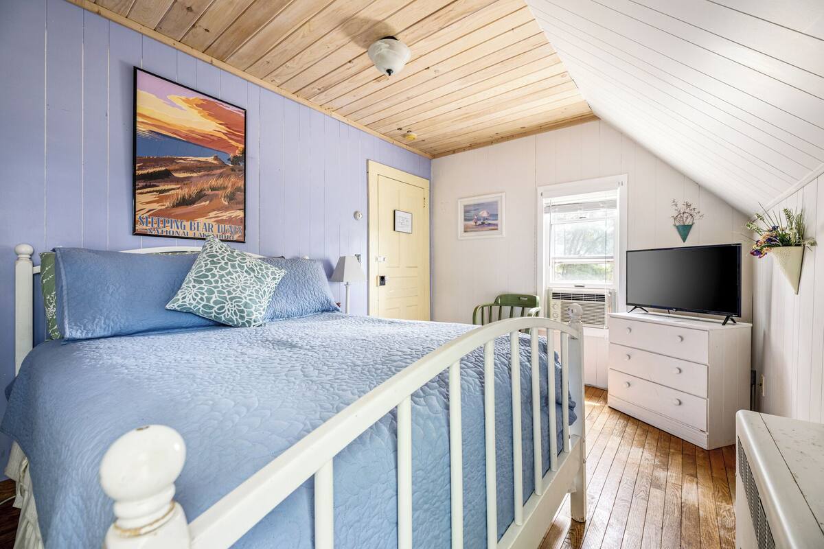 A bedroom with a bed, a dresser, a television, and a window.