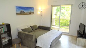Ein Schlafzimmer mit einem Bett, einem Sofa, einem kleinen Tisch mit Fernseher, einem Bücherregal und einem Bild von einer Strandlandschaft.