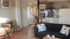 Moderni olohuone, jossa on musta sohva, puinen ruokapöytä ja tuolit. Kierreportaat johtavat ylemmälle tasolle.