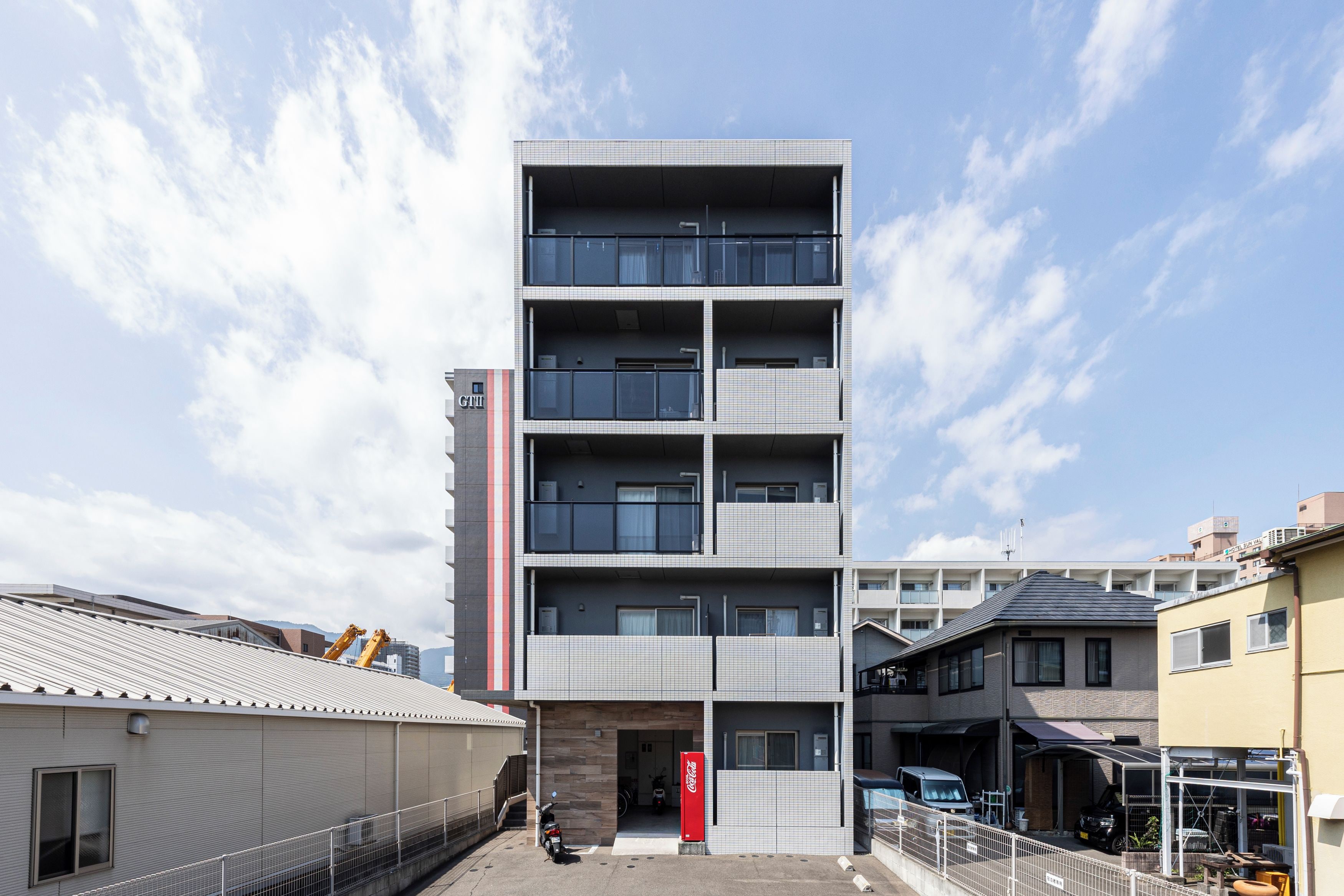 A multi-story building with a modern architectural design, featuring a central entrance, multiple balconies, and a visible Coca-Cola vending machine.