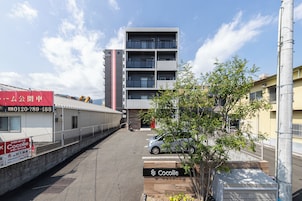 A multi-story building with a gated entrance, a parked car, and a tree in the foreground.