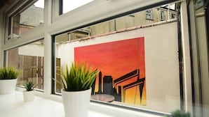 Ein Fenster mit Stadtbildgemälde und drei Blumentöpfen auf dem Fensterbrett.