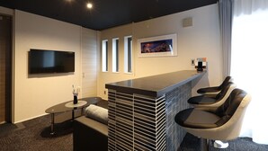 A modern hotel room with a flat-screen TV, a bar area with seating, a framed picture on the wall, and a window with curtains. - GRAND BASE Hakata City (Fukuoka)