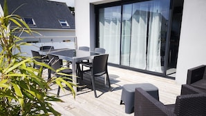 A patio with a glass table and chairs, a wicker sofa, and a sliding glass door. - Île Tudy: House with 3 terraces  (ile tudy)