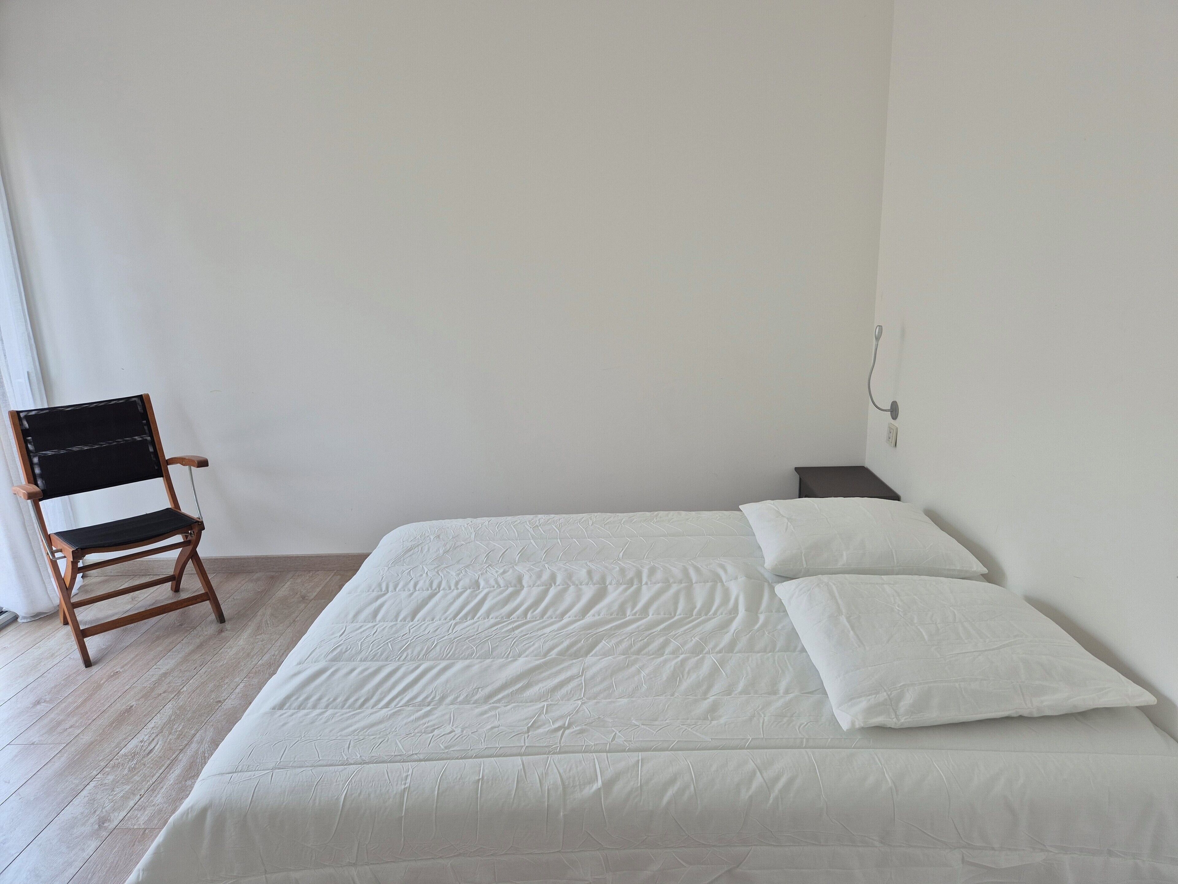 A bedroom with a bed, a chair, and a nightstand.