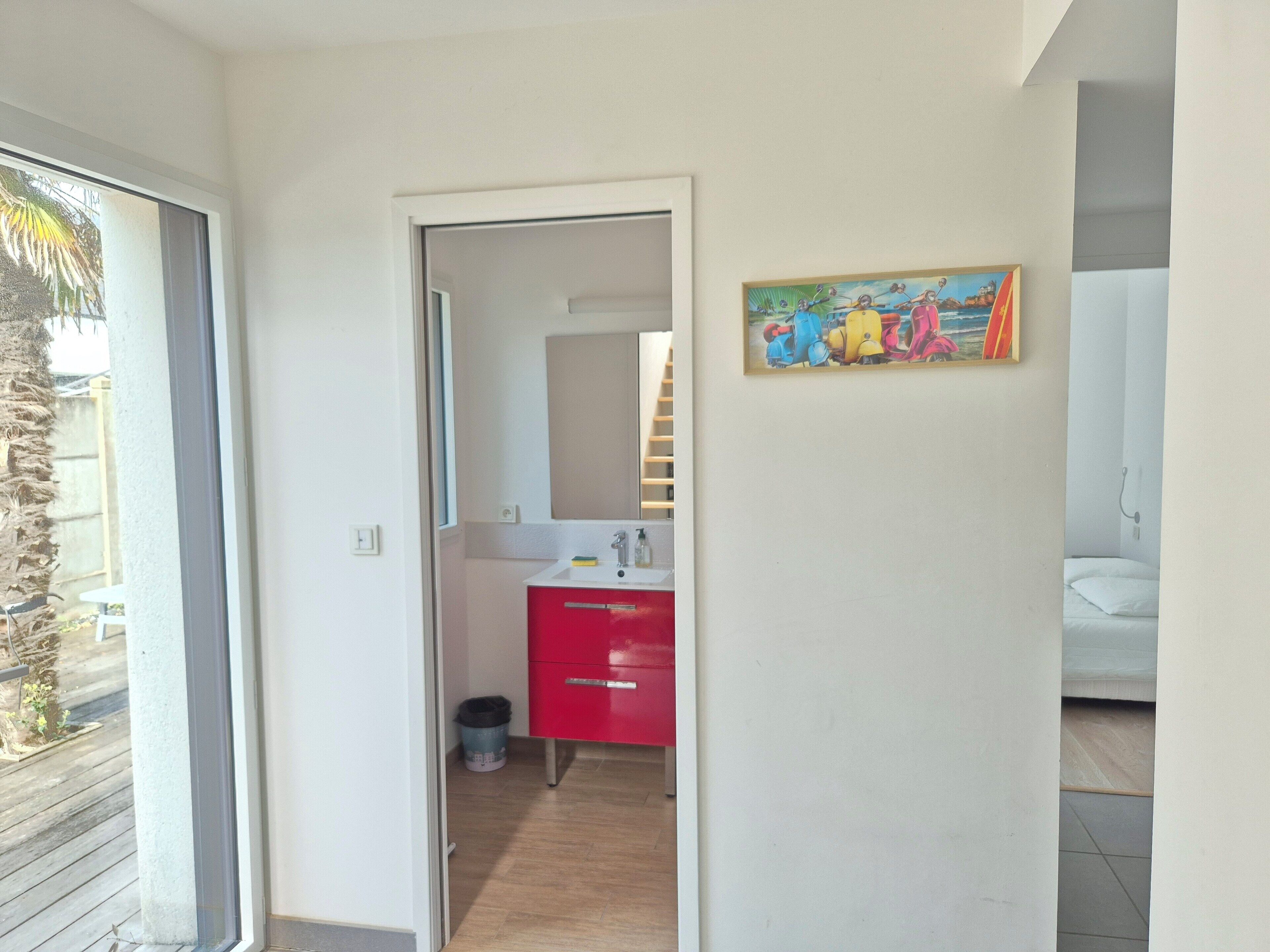 Een gang die leidt naar een badkamer met een rode kast en een schilderij aan de muur.