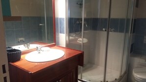 Une salle de bain avec un meuble-lavabo en bois, une cabine de douche en verre et des toilettes blanches.