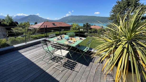 Une terrasse aménagée avec du mobilier d’extérieur, une table à manger pour deux personnes et une vue sur un lac et des montagnes en arrière-plan.