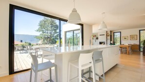Une cuisine moderne dotée d’un grand îlot central, de tabourets de bar, de luminaires suspendus et offrant une vue sur l’extérieur.