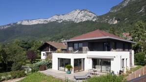 Une maison moderne à deux étages, dotée d’un balcon, de grandes fenêtres et offrant une vue sur les montagnes.