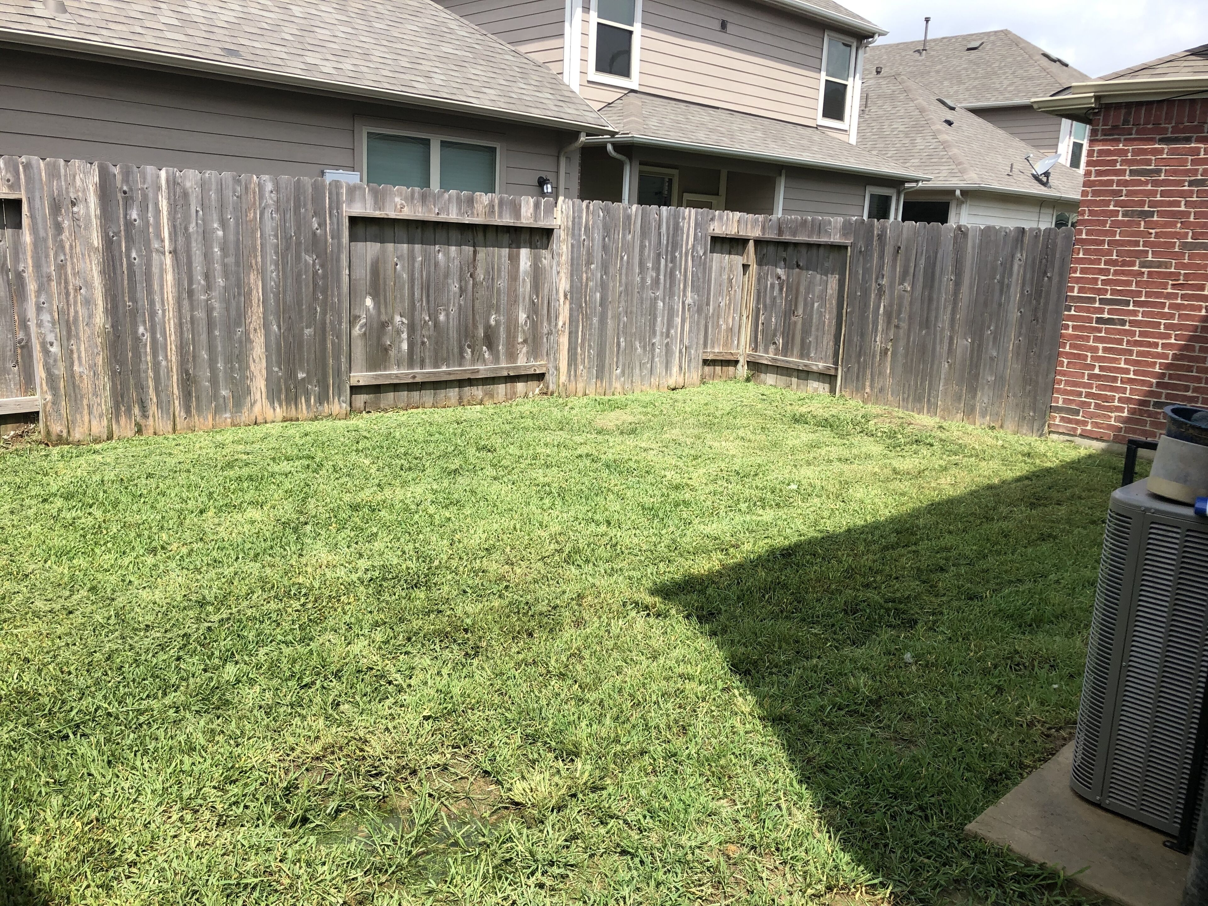 A backyard with a wooden fence, a grassy lawn, and a brick wall.