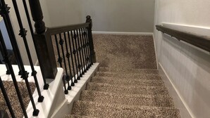 Eine Treppe mit hölzernem Geländer und einem an der Wand befestigten Kunstwerk, das eine sitzende Person zeigt.