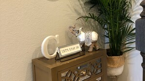Ein dekorativer Konsolentisch mit einem Schild, auf dem 'LET'S STAY IN' steht, einem Spiegel mit goldener Rahmen und einer Topfpflanze.