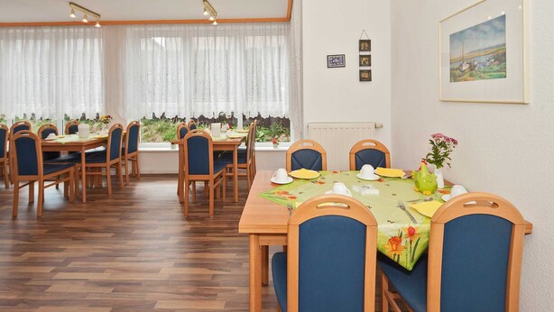 Un comedor con mesas y sillas de madera, vistas a la vegetación a través de amplias ventanas y cuadros en la pared.
