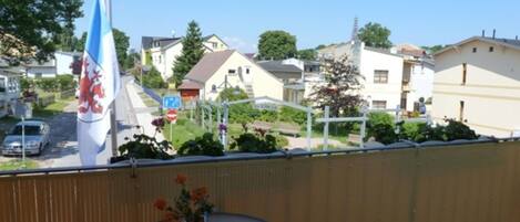 Ein Balkon mit einer Flagge, einem kleinen Tisch mit Schale und Blumen sowie einem Stuhl.