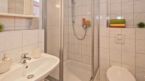 Un baño moderno con ducha envuelta en vidrio, lavamanos blanco y retrete.