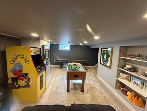 Une pièce équipée d’un baby-foot, d’une borne d’arcade Pac-Man et d’étagères remplies de souvenirs sportifs.