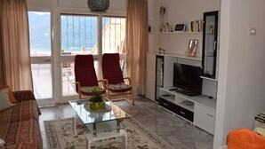 Un salon avec un canapé, deux fauteuils rouges, une table basse en verre, un téléviseur et une bibliothèque.