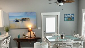 Een eethoek met een tafel, stoelen, een plafondventilator en een schilderij van boten aan de muur.