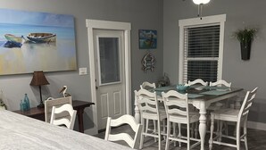 Een eethoek met een witte tafel en stoelen, een plafondventilator en een schilderij van boten aan de muur.