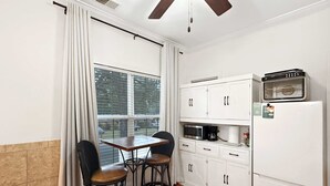 Une cuisine compacte avec un coin repas, comprenant une table avec deux chaises, un four à micro-ondes, une machine à café et un réfrigérateur.
