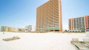 Un hôtel en bord de mer, avec plusieurs étages, une plage de sable au premier plan et d’autres bâtiments en arrière-plan.