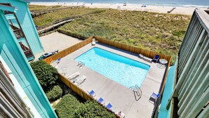 Zwembad op het dak met uitzicht op het strand, omgeven door een houten terras en ligbedden.