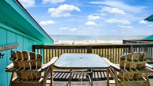 Een houten terras met tafel en stoelen, met uitzicht op een strand.