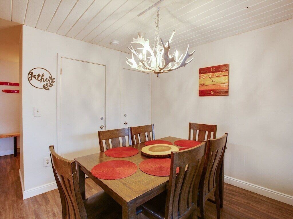 A dining area with a wooden table, red placemats, and a chandelier.