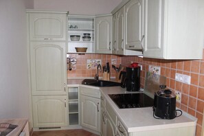 A kitchen with white cabinets, a black coffee maker, and a tiled backsplash. - Potthoff Vacation Rental - GM 69677 - Potthoff Vacation Rental (Graal-Müritz)