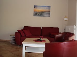 A red sofa, a white coffee table, and a painting of a sunset on the wall.