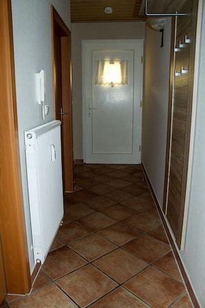 Um corredor com um radiador, uma porta com luminária e piso revestido de azulejos.