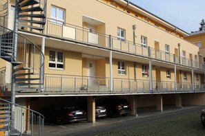 En byggnad med flera våningar, en central trappa, balkonger och en parkeringsplats med bilar.