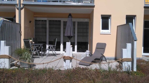 Un bâtiment doté d’un espace extérieur abrité, comprenant des tables, des chaises et un fauteuil.