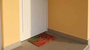 Ein Flur mit einer weißen Tür, einer Fußmatte und einem Lichtschalter an der Wand.