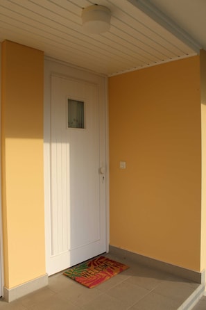 Um corredor com uma porta branca, um tapete de boas-vindas e um interruptor de luz na parede.