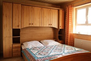 A bedroom with a wooden bed, a quilt, and built-in wooden cabinets. - Potthoff Vacation Rental - GM 69677 - Potthoff Vacation Rental (Graal-Müritz)