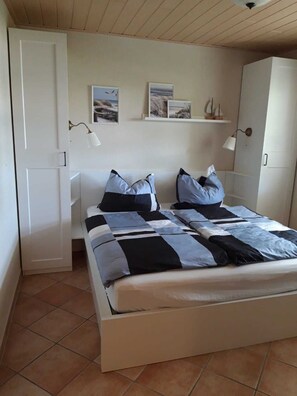 Une chambre à coucher avec un lit, deux lampes fixées au mur et une étagère avec des photos.