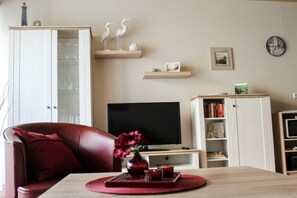 Uma sala de estar com televisão, sofá de couro vermelho, uma mesa de madeira com um vaso e uma estante de livros.