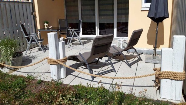 Ein Außenbereich mit Lounge-Möbeln, Tischen, einer Seilbarriere und einem Blumentopf.
