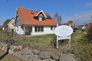 Une maison avec un toit recouvert de tuiles rouges, une enseigne et un mur de pierre au premier plan.