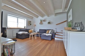 A modern living room with a grey sofa, wooden flooring, a small table, and a staircase leading to an upper level.