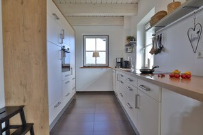 Une cuisine avec des meubles blancs, un banc en bois, une fenêtre et un évier.