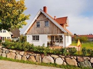 A wooden house with a sloped roof, a stone wall in front, and a grassy yard. - Serenity island vacation home (Kalkhorst)