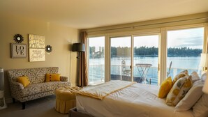 A bedroom with a large bed, a sofa, and a view of a lake through large windows. - Stellamar on Hayden, Close-in Executive Waterfront (Hayden)